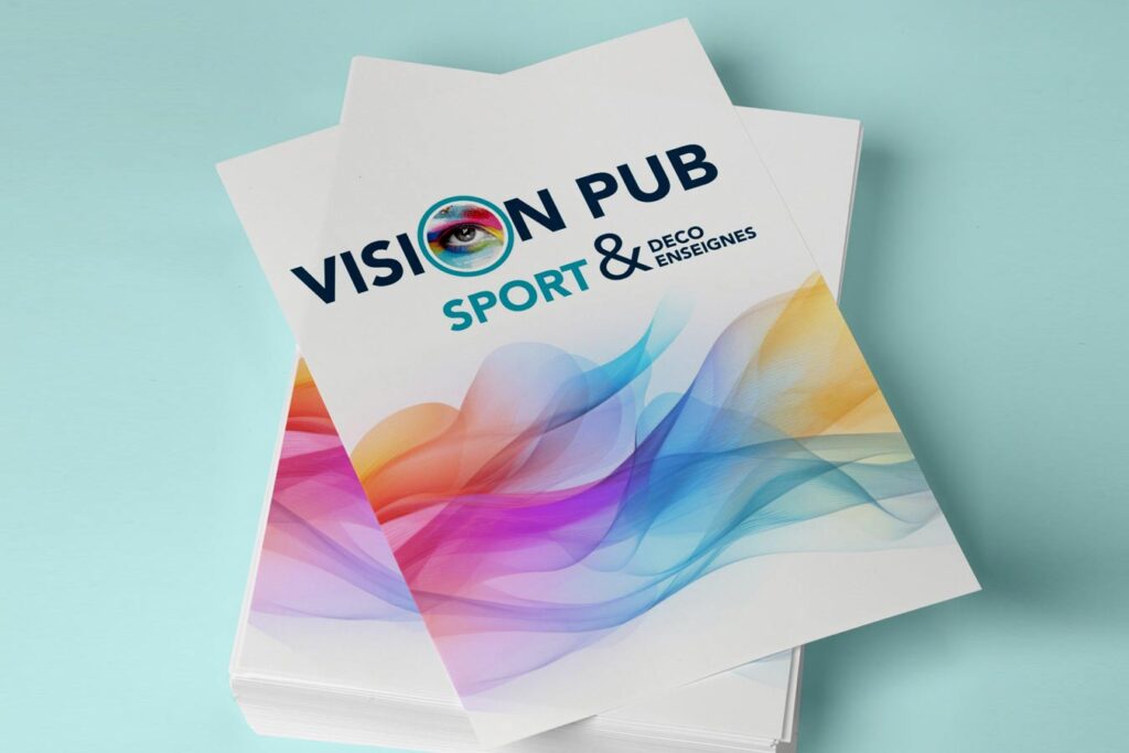 Pile de brochures blanches "VISION PUB" sur fond bleu clair. Le logo inclut un œil coloré et le texte "SPORT & DECO ENSEIGNES".