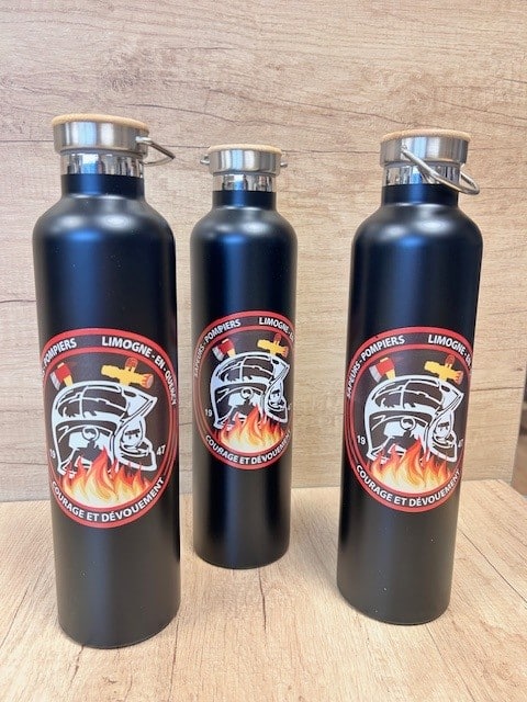 Trois gourdes noires avec bouchon bois et inox. Chaque gourde arbore un logo rond pompier : casque, haches, flammes, et les textes "SAPEURS-POMPIERS LIMOGNE-EN-QUERCY 19 47" et "COURAGE ET DÉVOUEMENT".